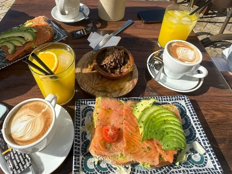 Breakfast on a terrace table: salmon and avocado toast on a mosaic plate, two coffees and orange juice