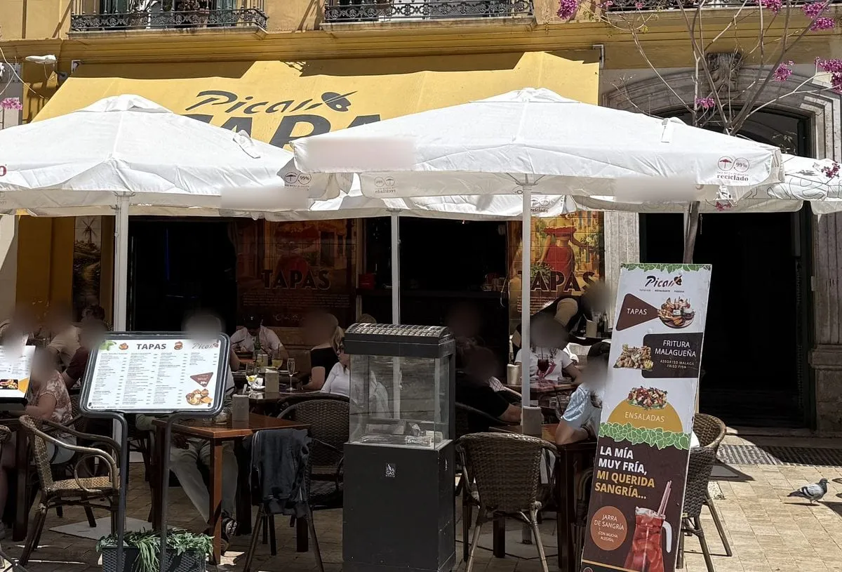 The terrace of Picas Brunch & Tapas on Plaza de la Merced: white parasols under the yellow awning with the Picas logo and the word TAPAS